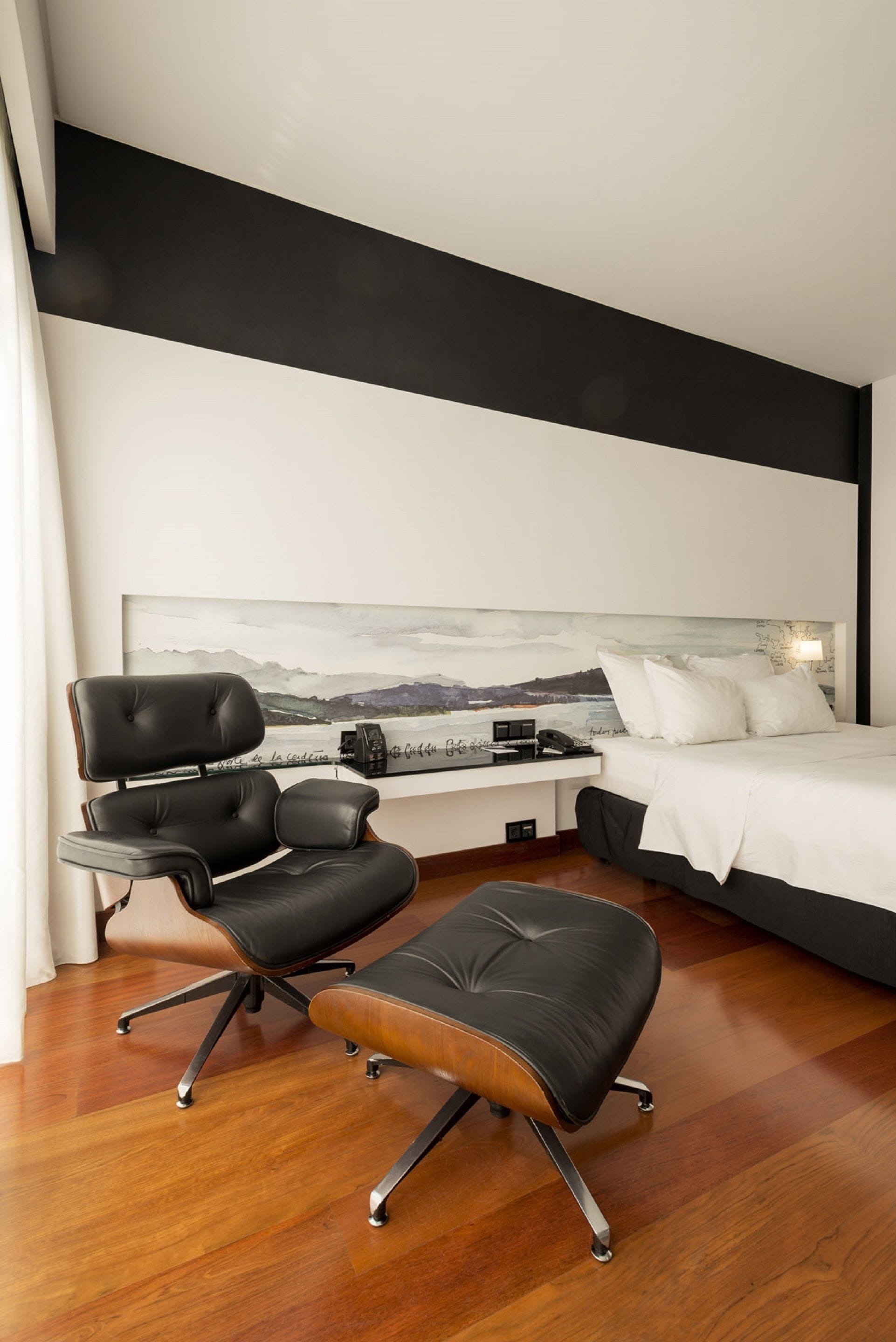 Una habitación de hotel moderna con una cama grande, un escritorio con silla y un cuadro en la pared.