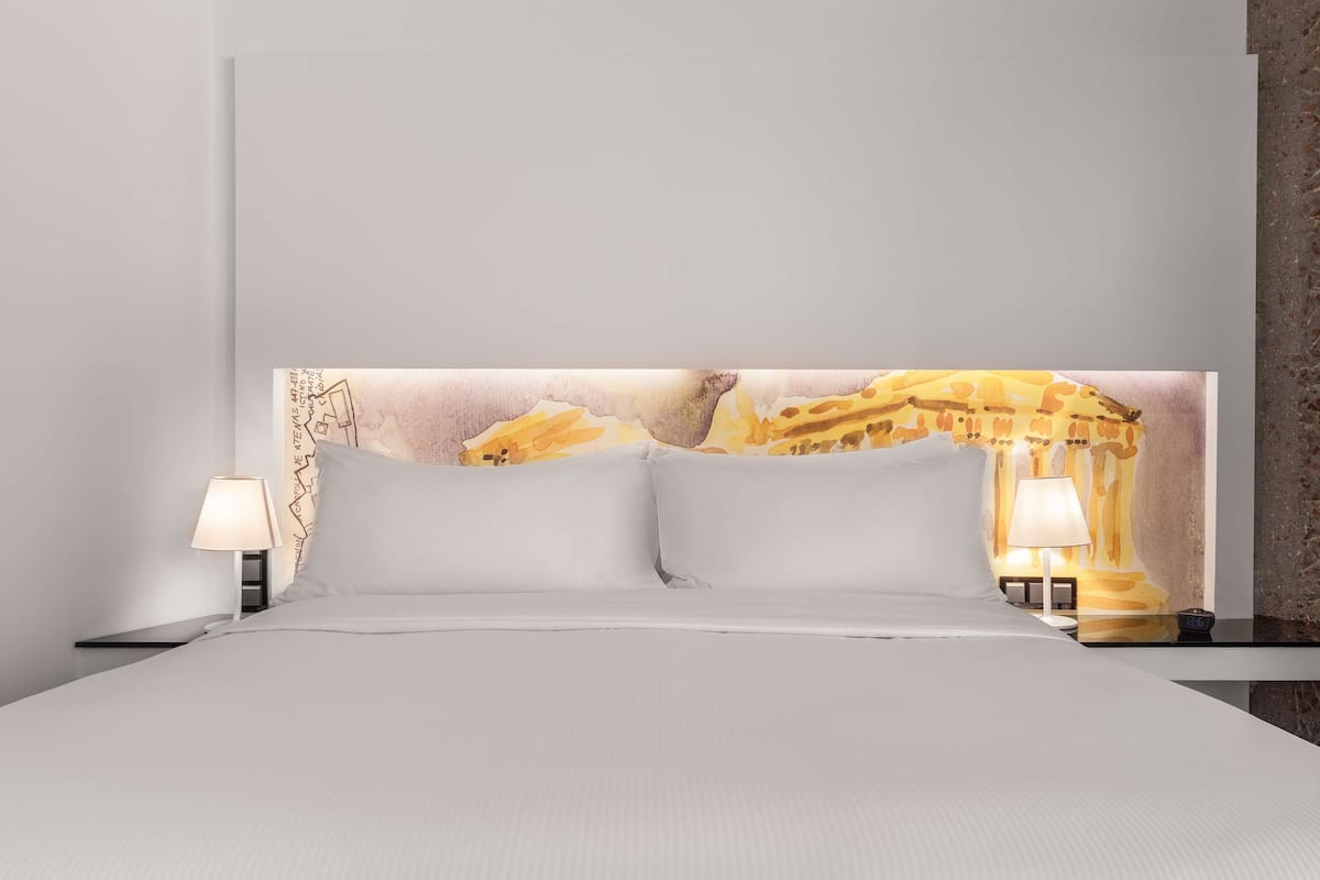 Een hotelkamer met een groot bed, twee nachtkastjes met lampen, en een muurschildering.