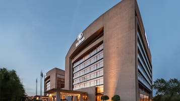 Un hotel moderno con un llamativo logotipo de Hilton, varios pisos y una zona de acceso cubierta.