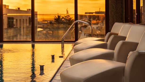 Un espace aménagé avec des sièges au bord de la piscine, offrant une vue sur le coucher de soleil au-dessus de la ville.
