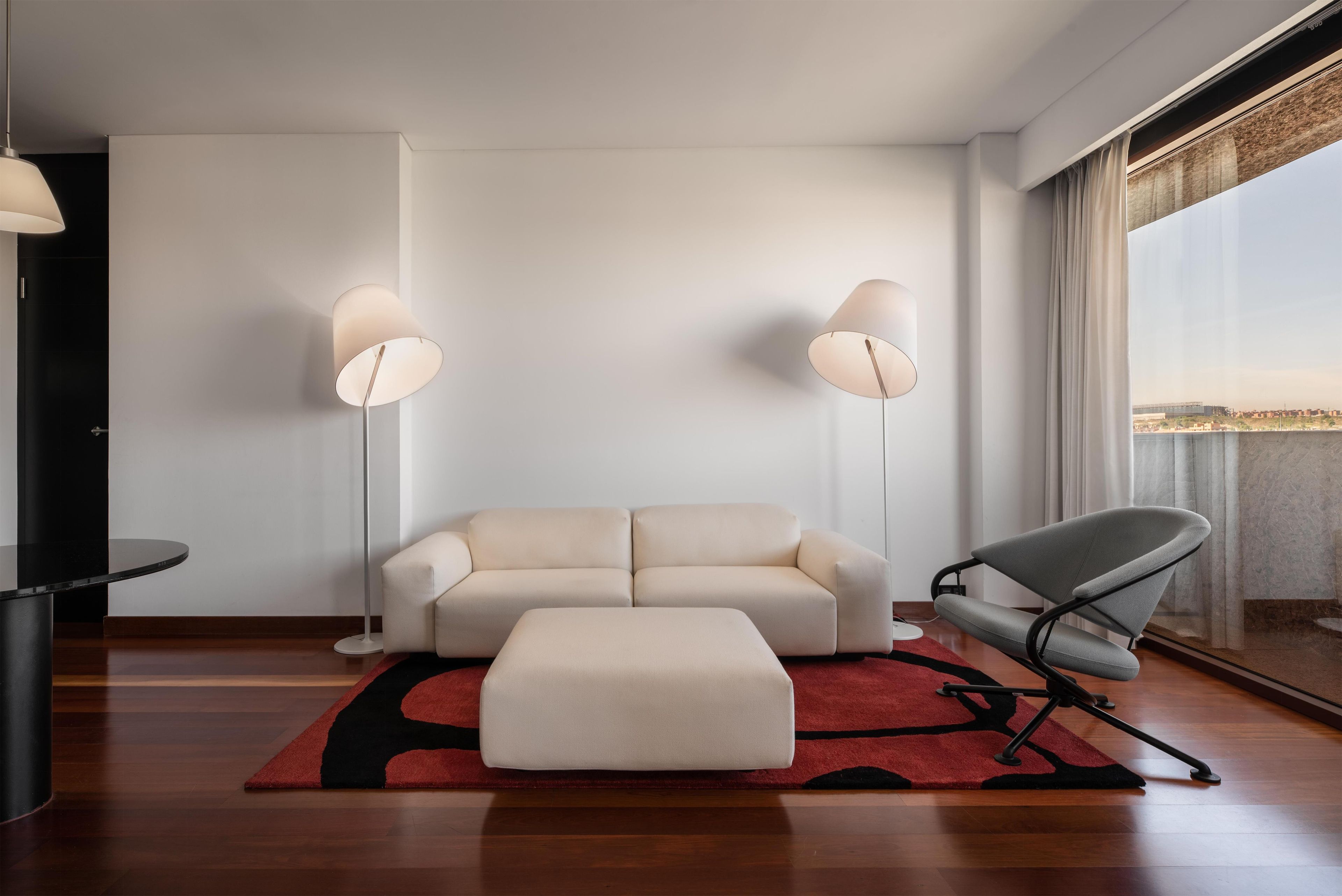 Ein modernes Wohnzimmer mit einer Couch, einem Hocker, einer Stehlampe und einem Sessel.