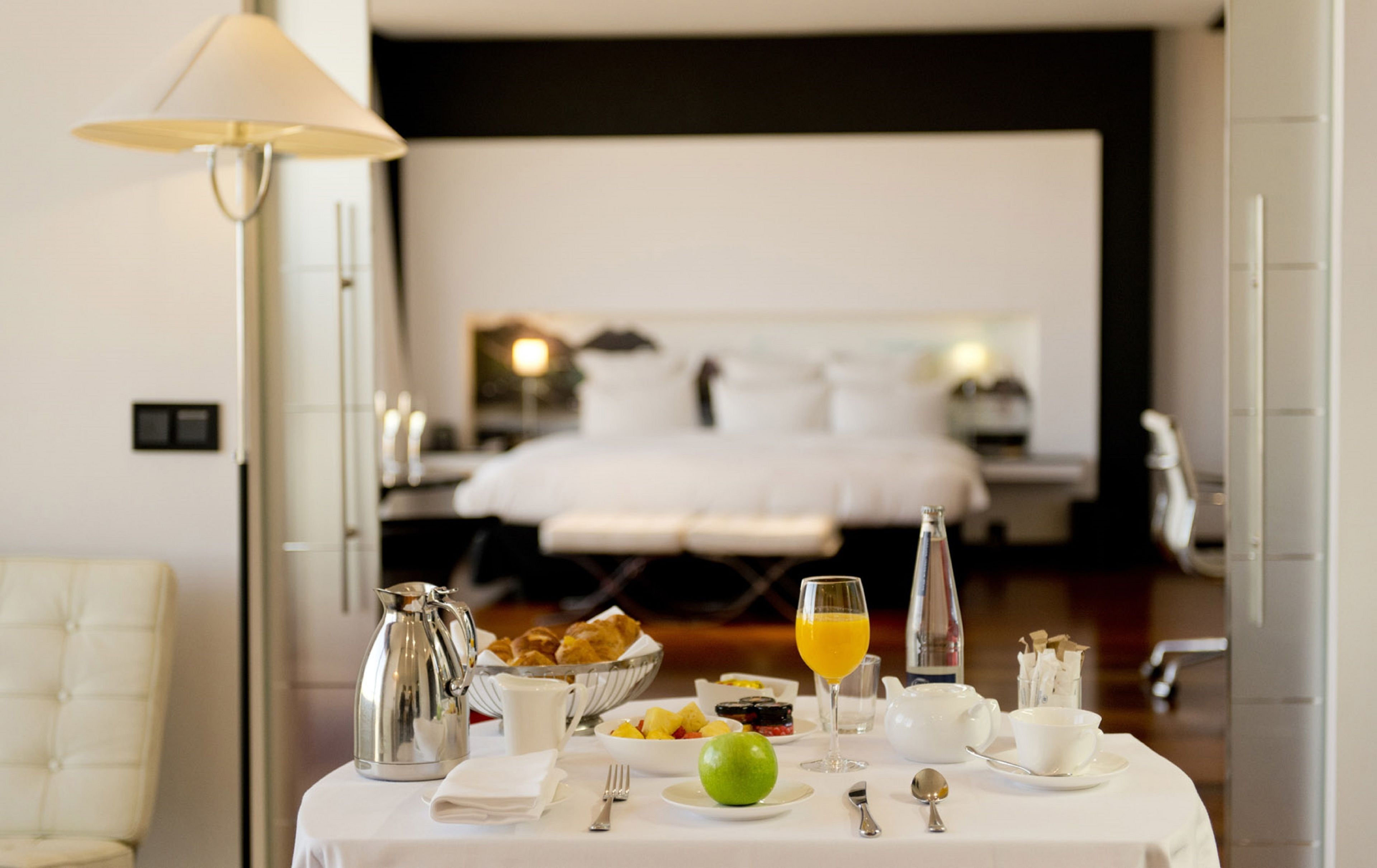 A breakfast table with a pitcher, bowl, fruit, and a glass of orange juice in a hotel room.