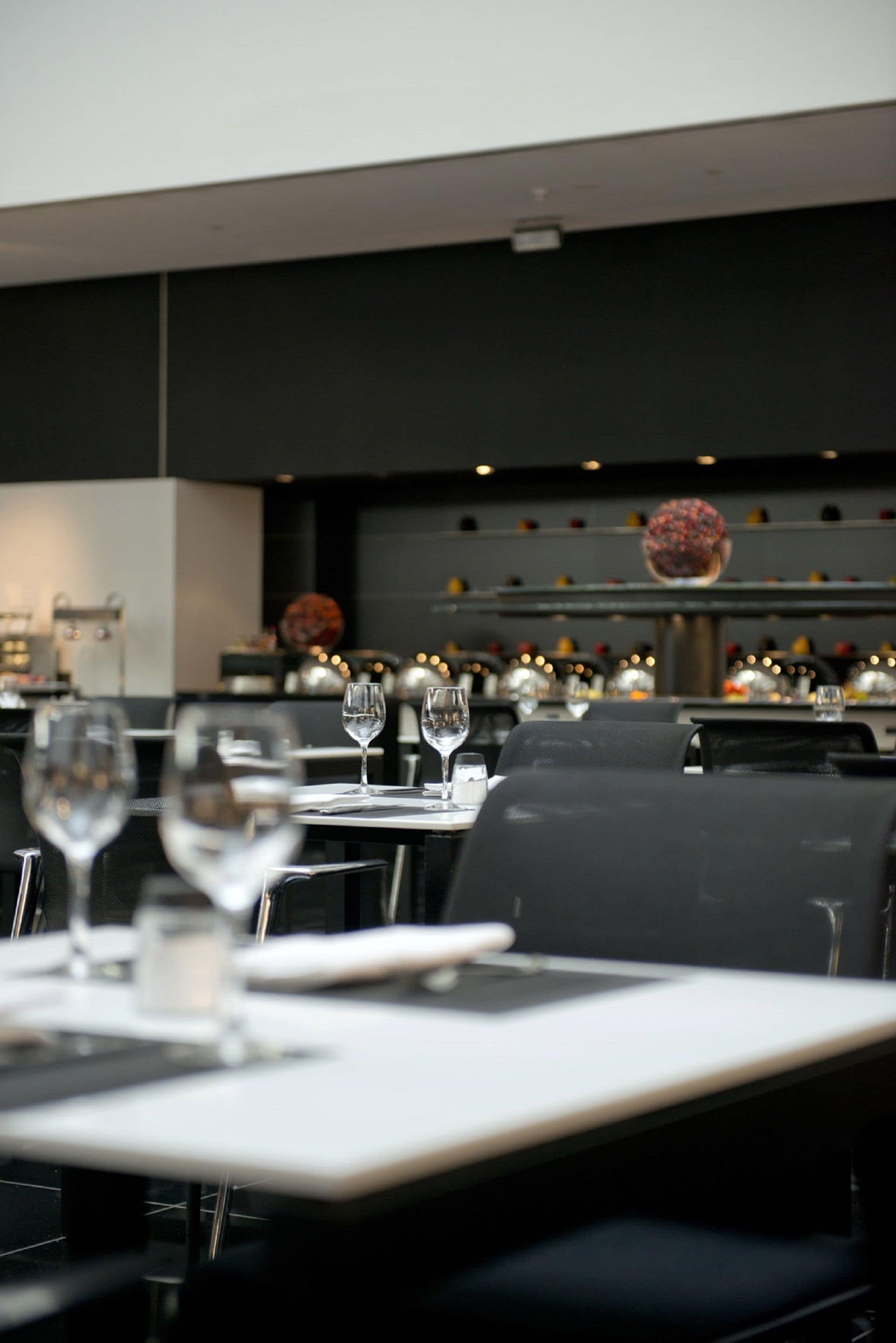 L’intérieur d’un restaurant, avec des tables dressées pour le service, un espace cuisine en arrière-plan et un saladier décoratif rempli de fruits accroché au mur.