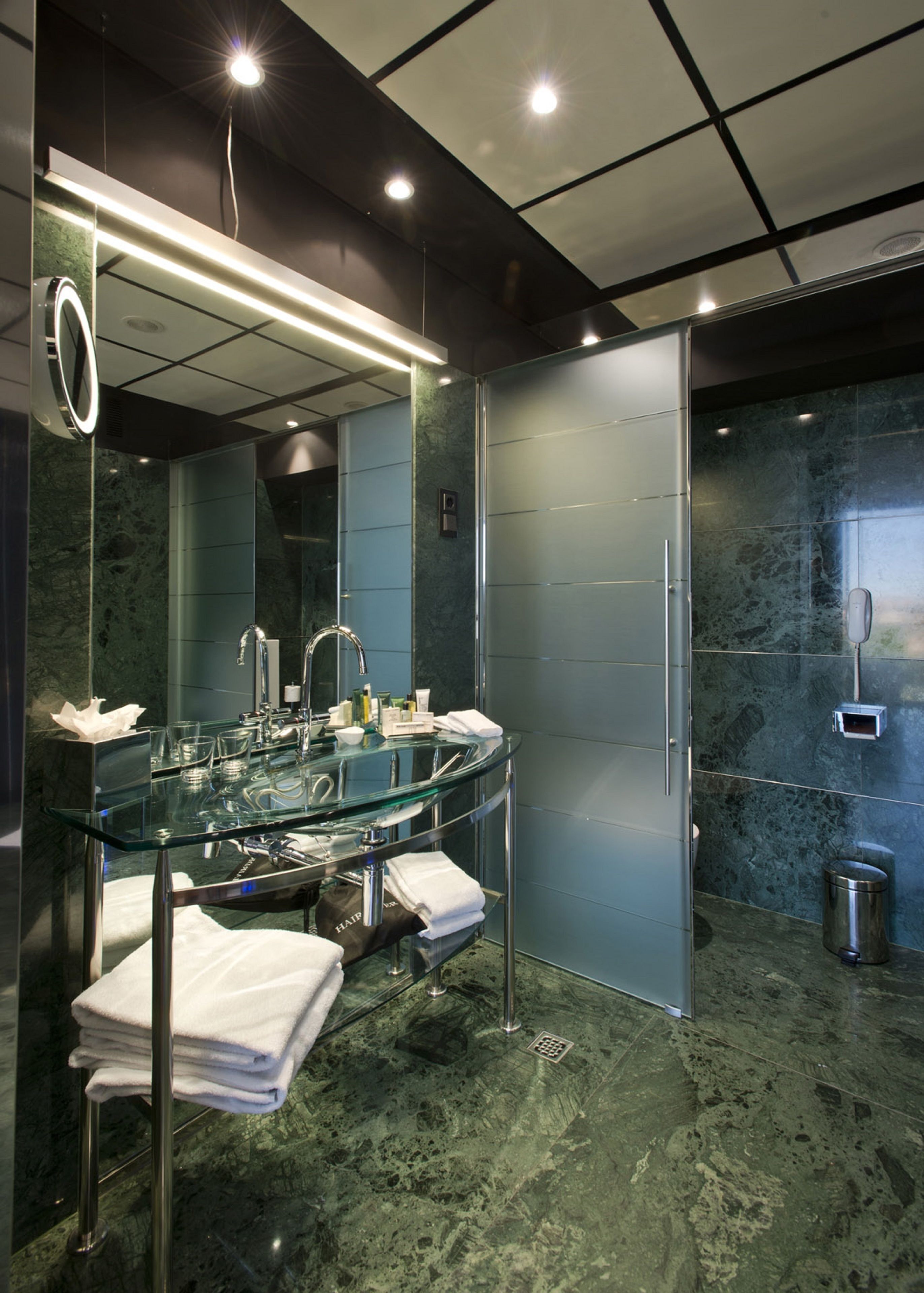Un baño moderno con lavamanos de vidrio, un espejo grande y un separador de vidrio esmerilado.