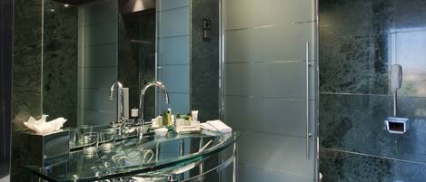 A modern bathroom with a glass sink, a large mirror, and a frosted glass partition.