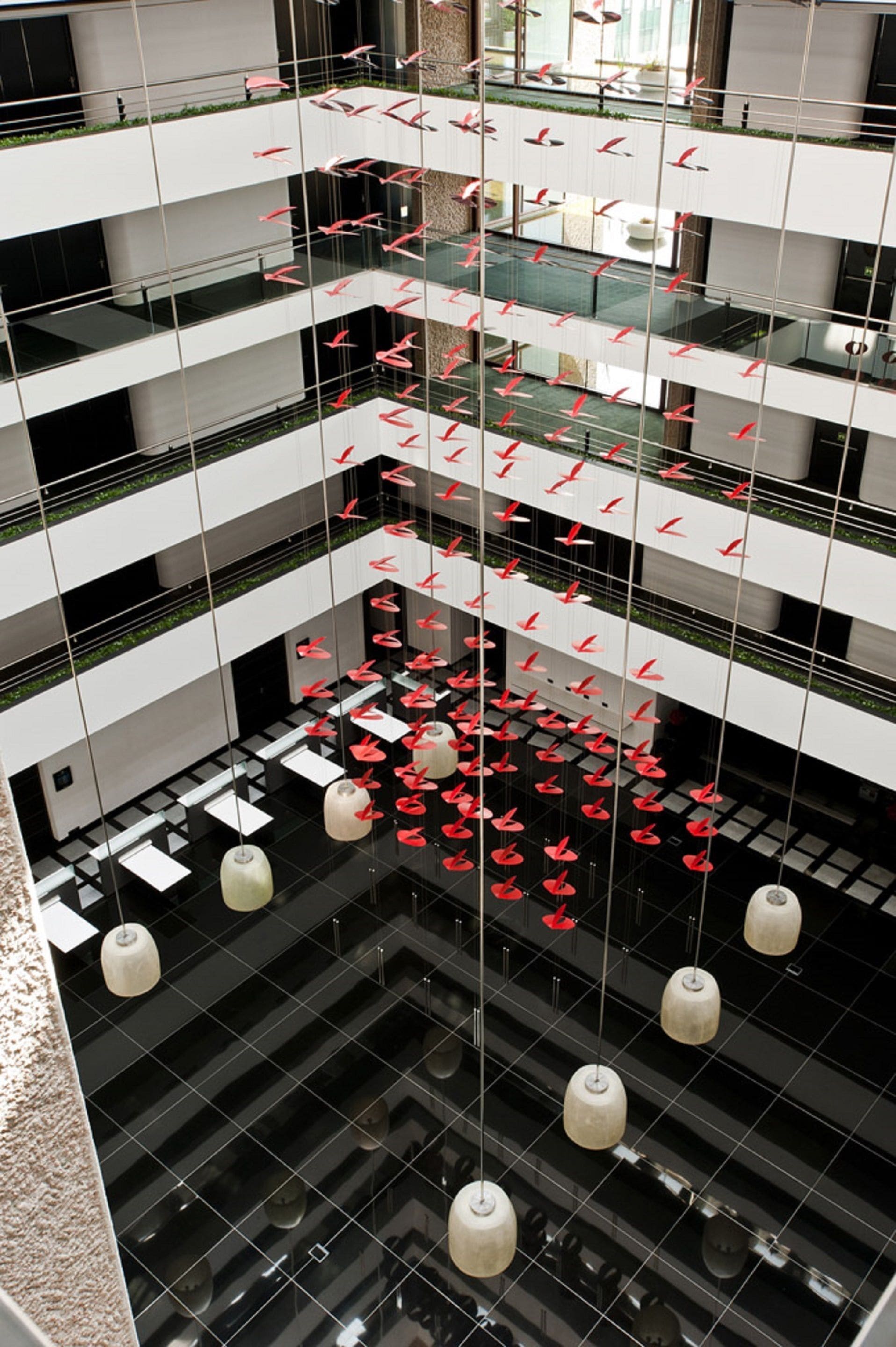 Ein mehrgeschossiges Atrium mit schwebenden roten Stühlen und Pendelleuchten.
