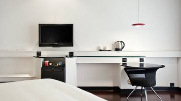 Ein modernes Hotelzimmer mit Bett, Schreibtisch mit Computer, Fernseher und Kaffeemaschine.