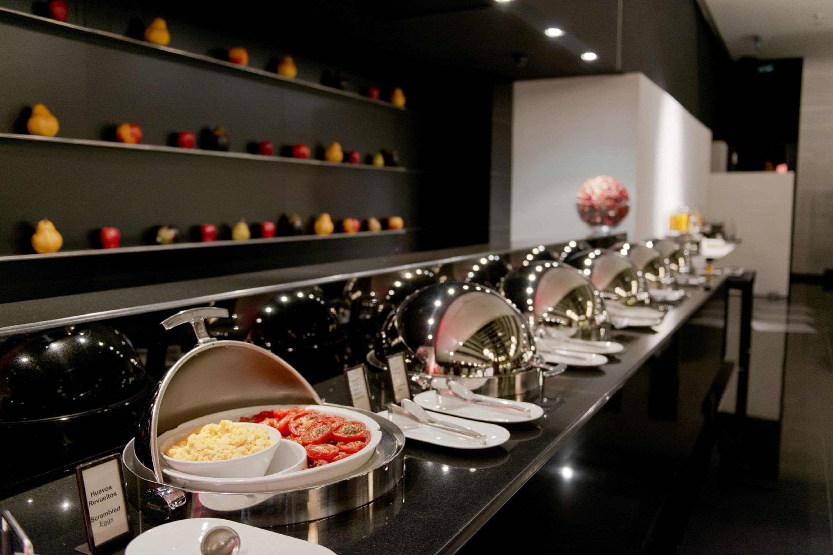 A buffet line with various food items and a display of fruits on shelves.