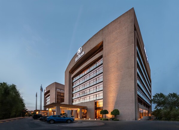 A modern hotel with a prominent Hilton logo, multiple floors, and a covered entrance area. - Hilton Madrid Airport (Madrid)