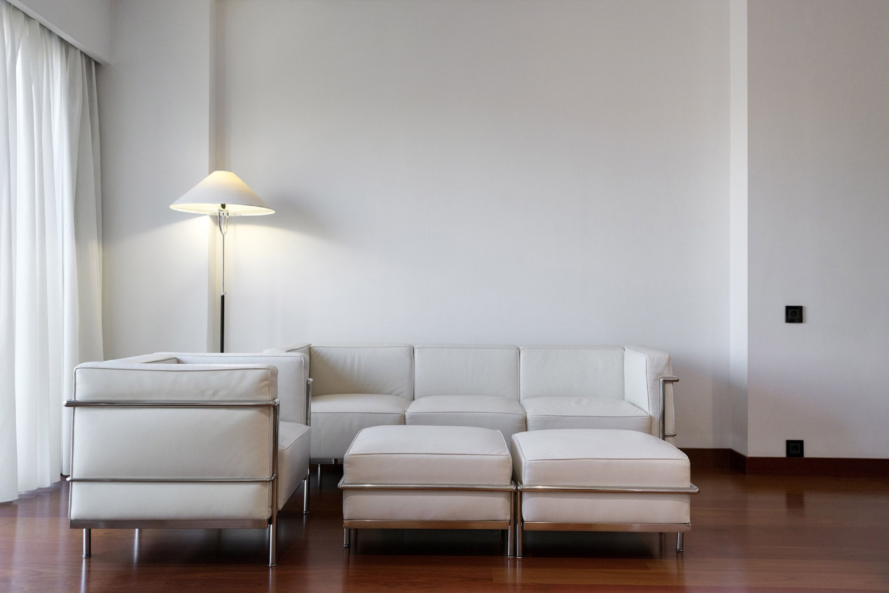 Un moderno salón con un sofá de cuero blanco y otomanas, una lámpara de pie y suelo de madera.