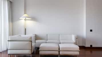Un moderno salón con un sofá de cuero blanco y otomanas, una lámpara de pie y suelo de madera.