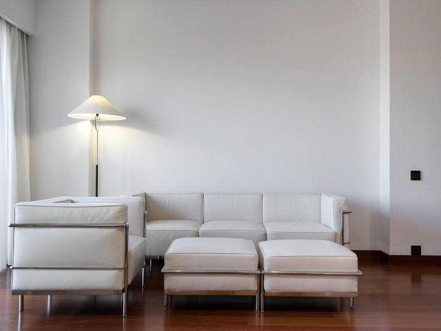 Un moderno salón con un sofá de cuero blanco y otomanas, una lámpara de pie y suelo de madera.
