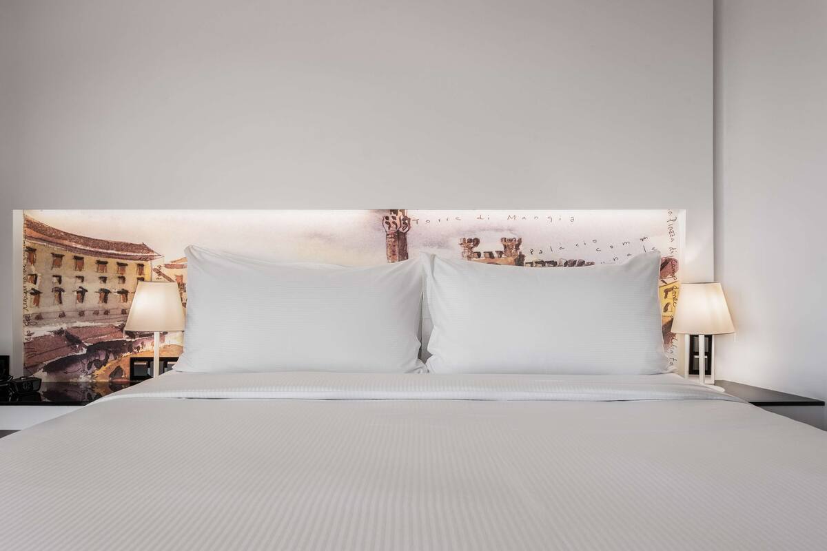 Een hotelkamer met een bed, twee bedlampen en een muurschildering van een stadsgezicht.