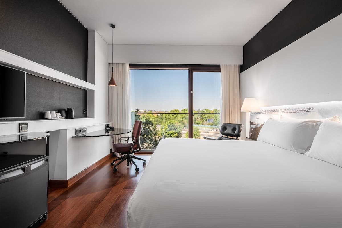 Een moderne hotelkamer met een groot bed, een bureau met stoel, een aan de muur bevestigde televisie en een balkon met uitzicht.