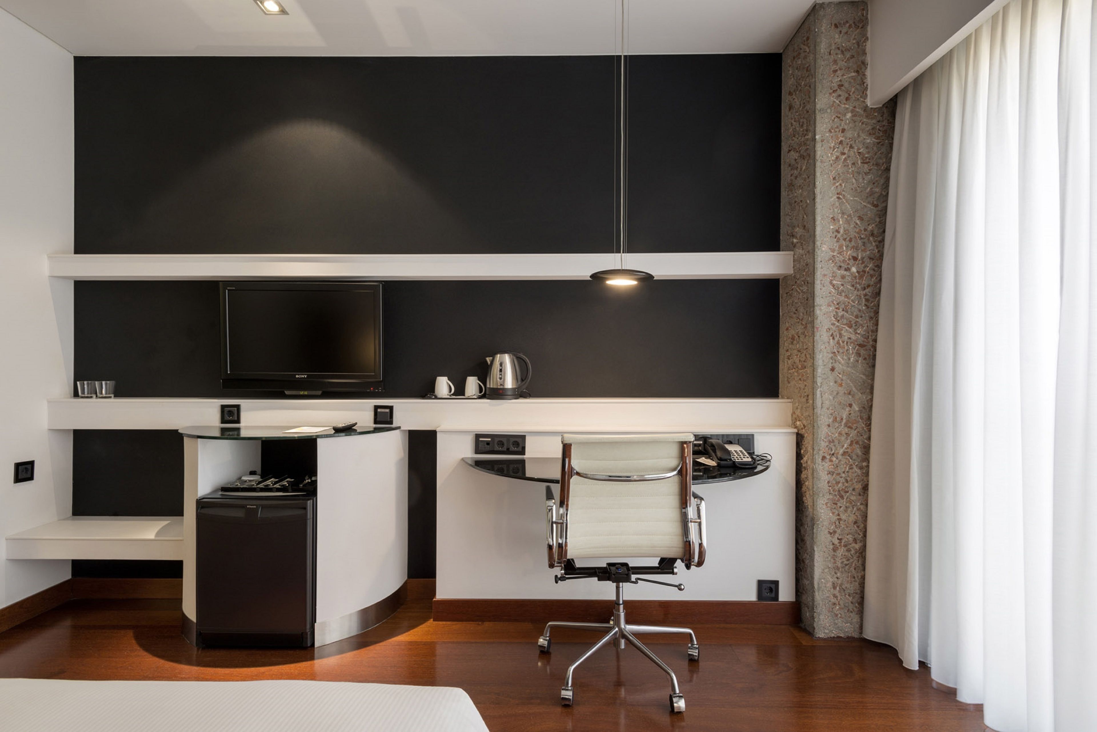 Una habitación de hotel moderna con una paleta de colores blanco y negro, un televisor de pantalla plana, un escritorio con una silla y un mini bar.
