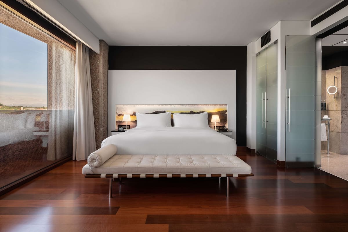 Een moderne slaapkamer met een groot bed, een bankje en uitzicht op de omgeving.