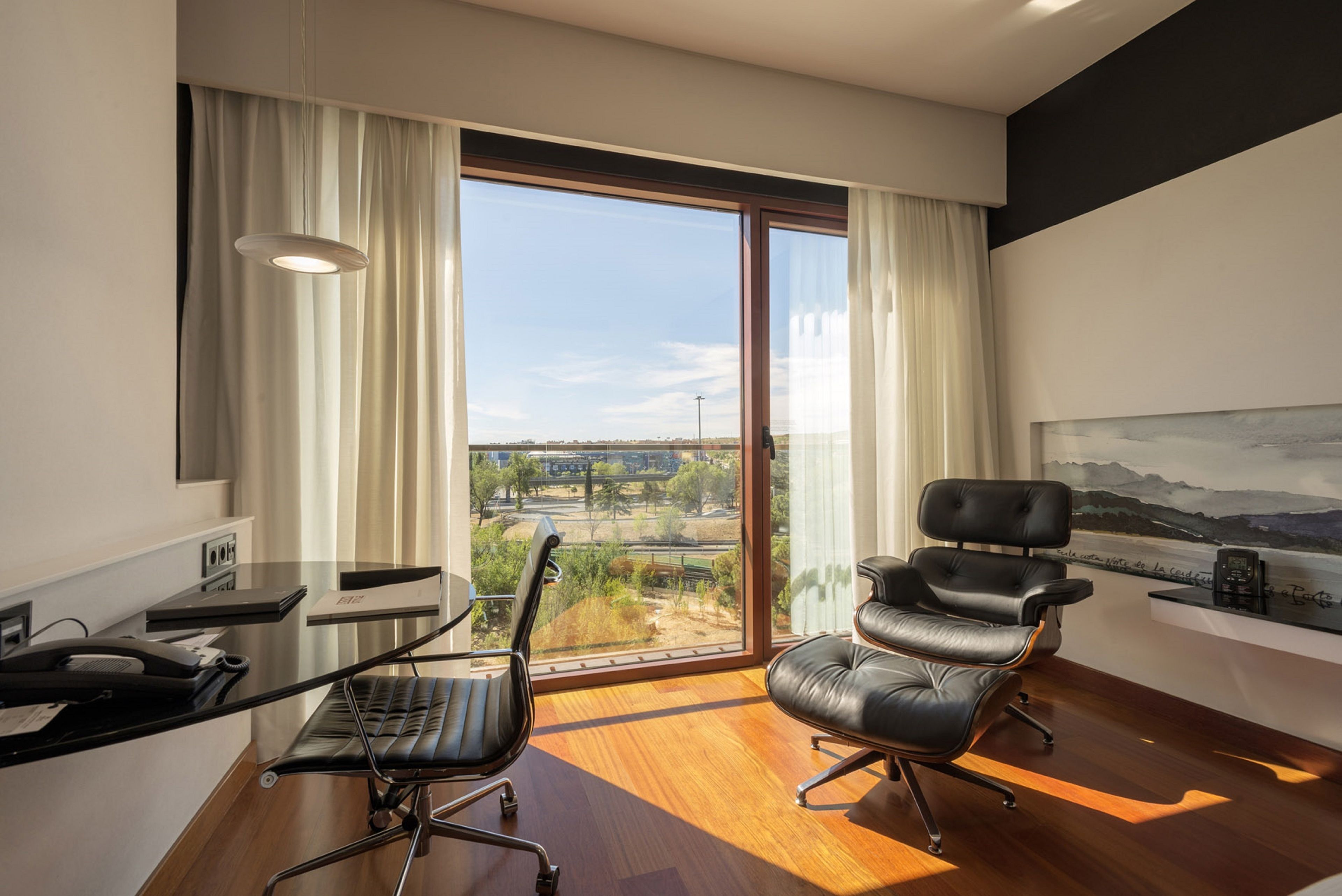 Un espace de bureau moderne comprenant un bureau, deux chaises, une grande fenêtre avec vue et un tableau accroché au mur.
