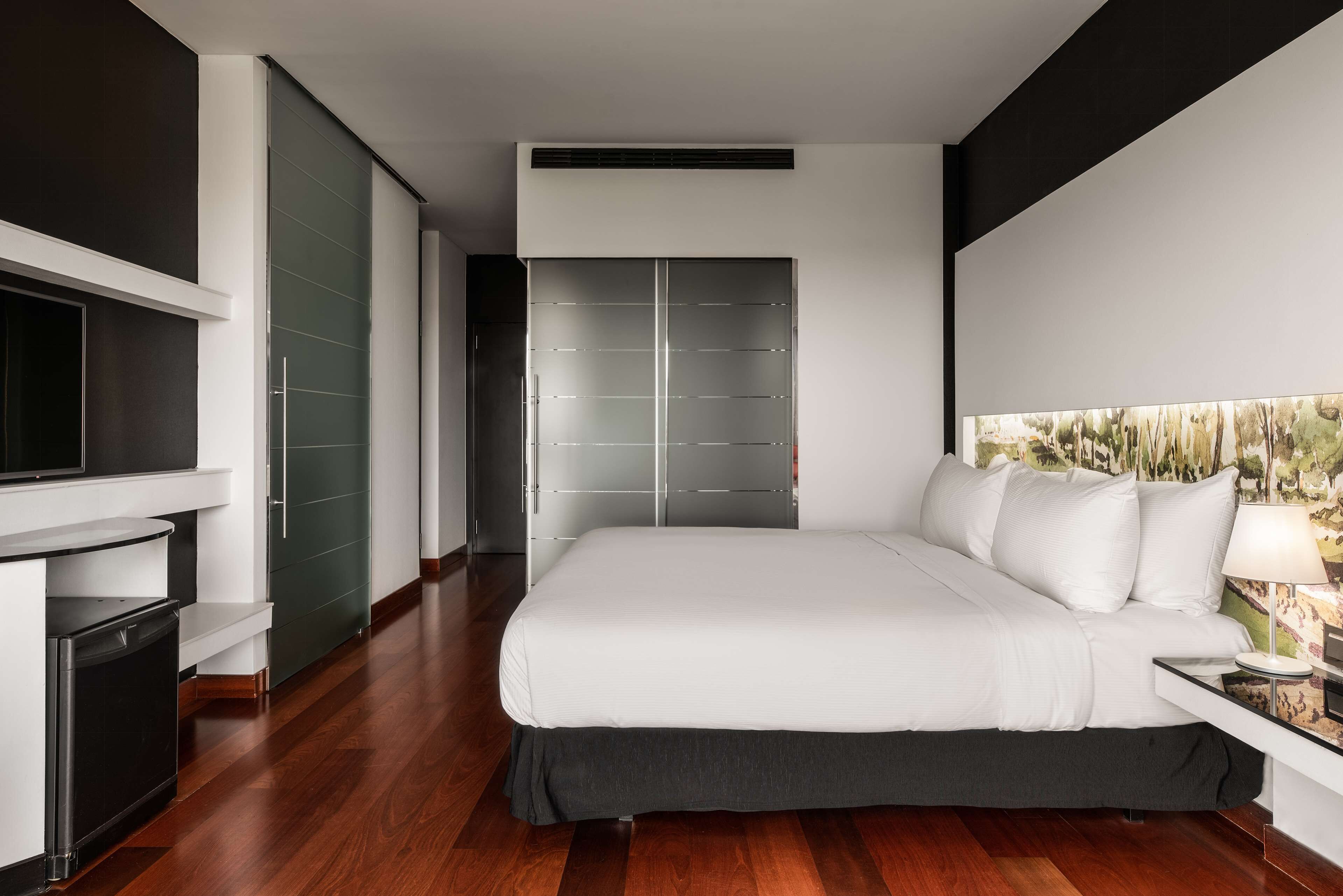 A modern bedroom with a large bed, a TV, a wardrobe, and a painting on the wall.