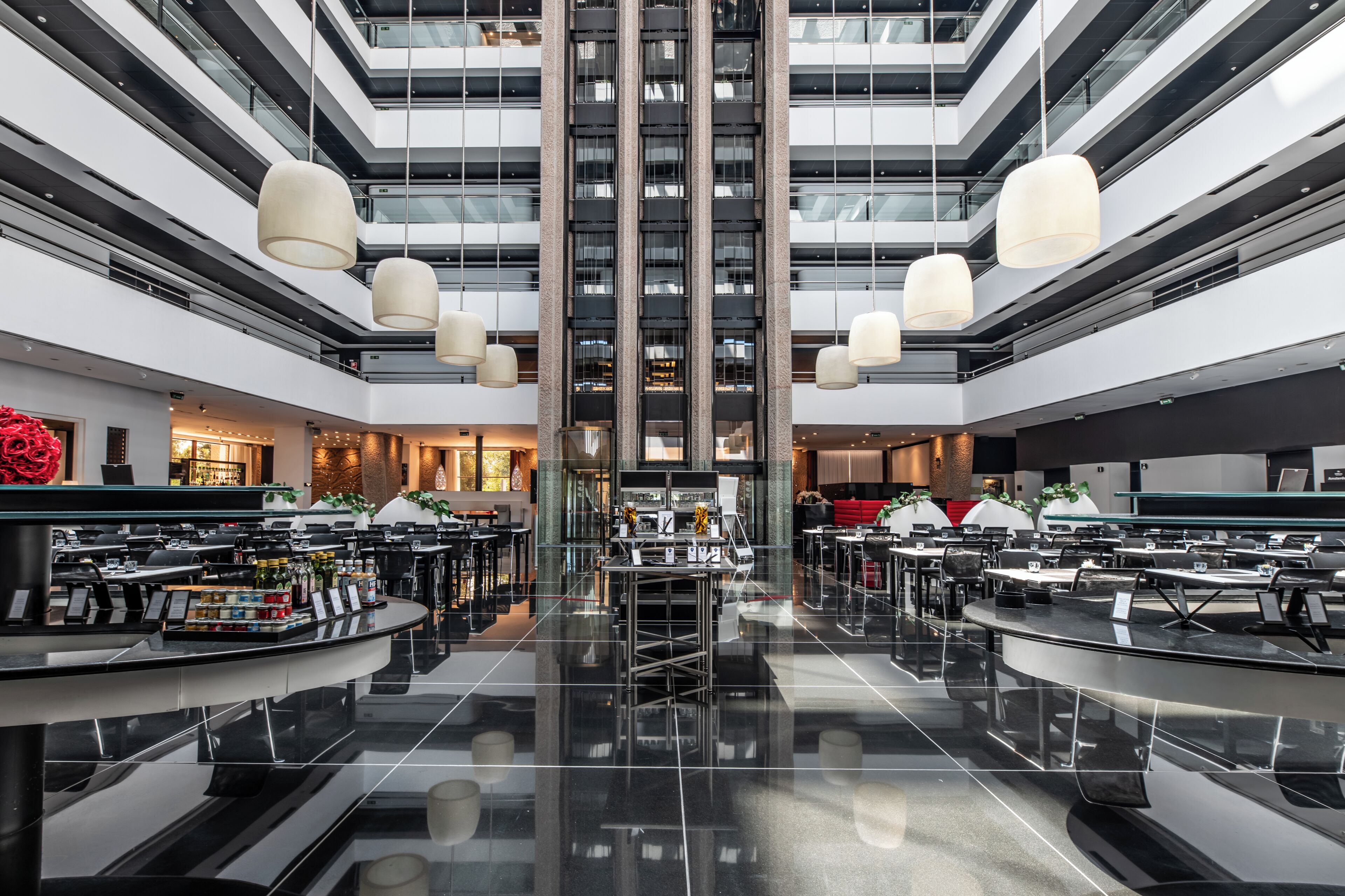 A modern hotel lobby with a central staircase, multiple dining areas, and a bar.