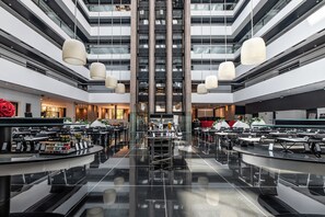 Un moderno vestíbulo de hotel con una escalera central, varias zonas de comedor y un bar.
