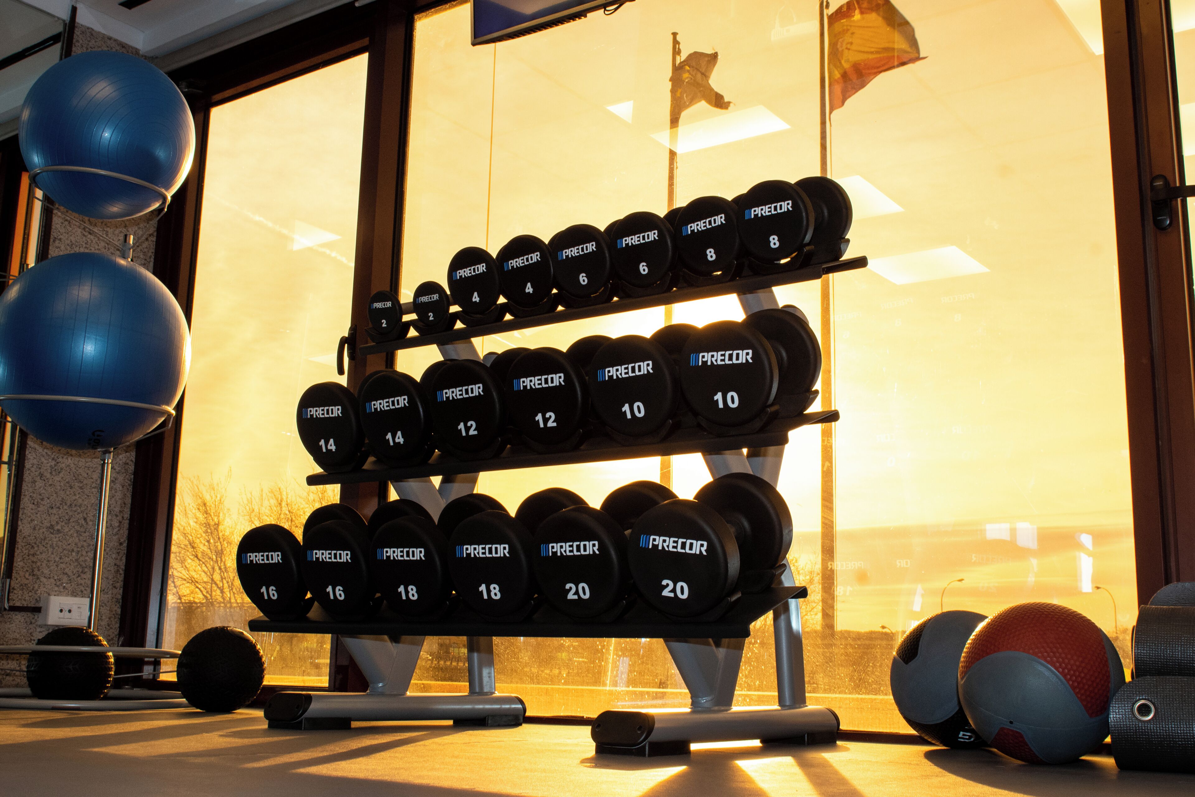 A gym with a rack of dumbbells, exercise balls, and a window with a view.