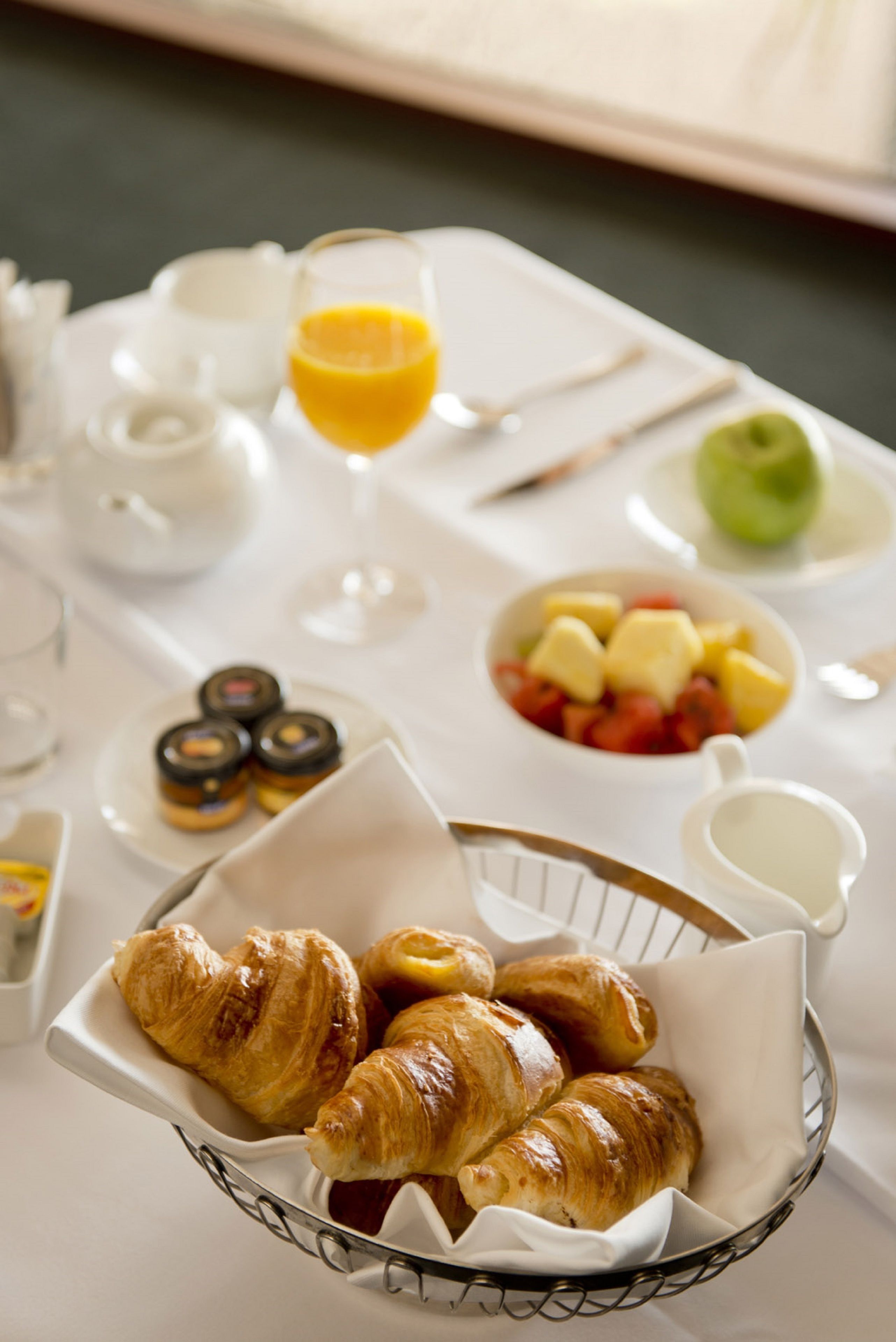 Un desayuno con cruasanes, fruta y jugo sobre una mesa.