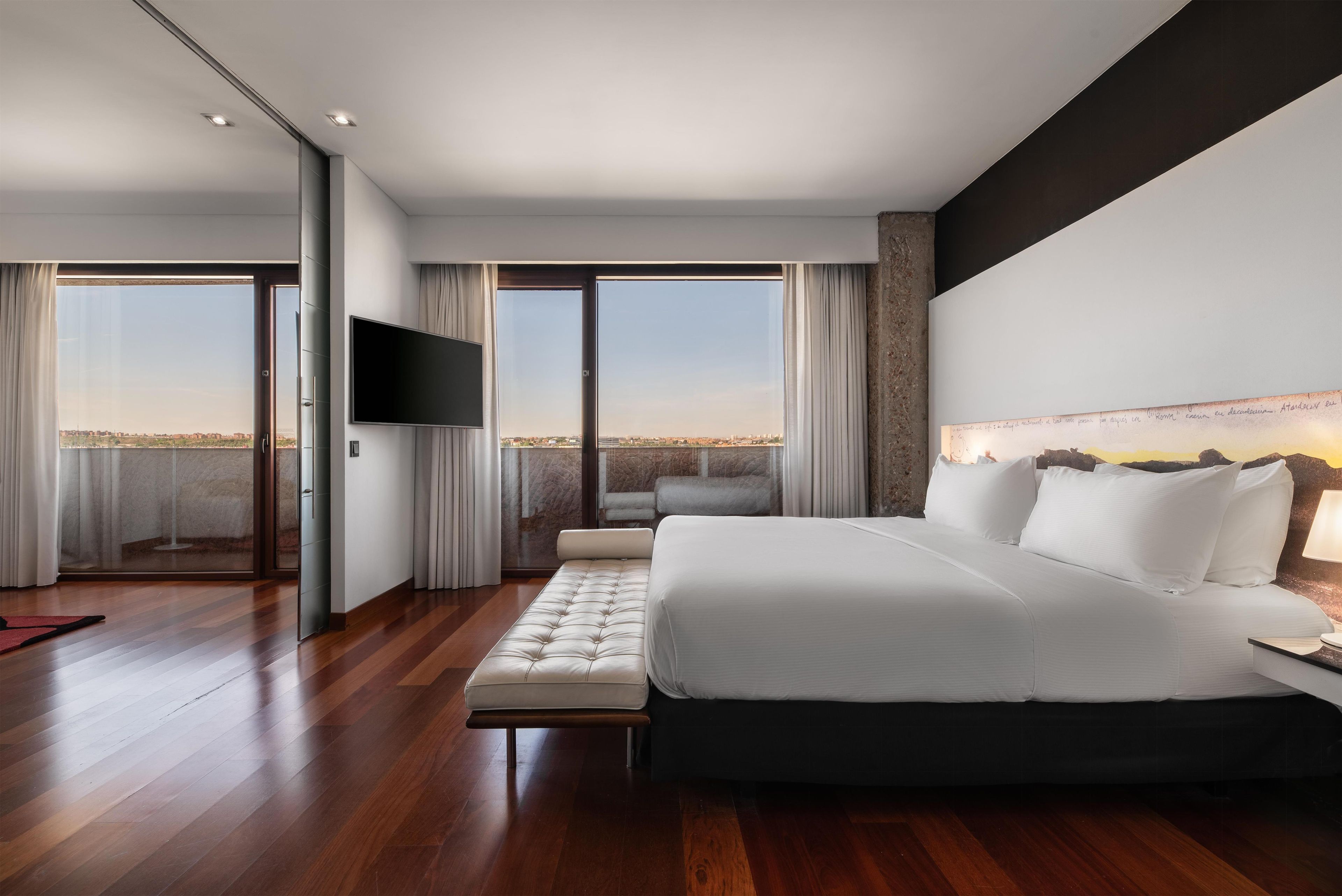 Una moderna camera d'albergo con un ampio letto, una TV a schermo piatto e vista sulla città.