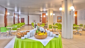 A spacious dining area with green chairs and tables, a buffet table with various food items, and a ceiling with recessed lighting. - Praia Dourada Hotel (Porto Santo)