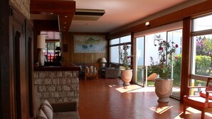 A spacious lobby with a stone wall, a large painting, and a seating area with a view of the outdoors. - Praia Dourada Hotel (Porto Santo)