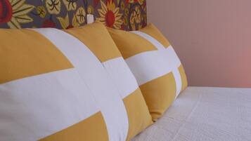 Una cama con dos almohadas, una amarilla y otra blanca, y un cabecero estampado con motivos florales.