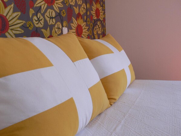 Una cama con dos almohadas, una amarilla y otra blanca, y un cabecero estampado con motivos florales.