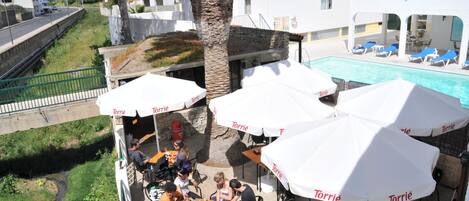 Un espacio al aire libre con sombrillas, una piscina y vistas a una calle residencial.