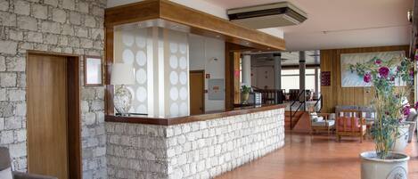 A lobby with a stone wall, a reception desk, and a seating area with chairs and a large potted plant.