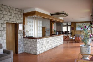 A lobby with a stone wall, a reception desk, and a seating area with chairs and a large potted plant. - Praia Dourada Hotel (Porto Santo)