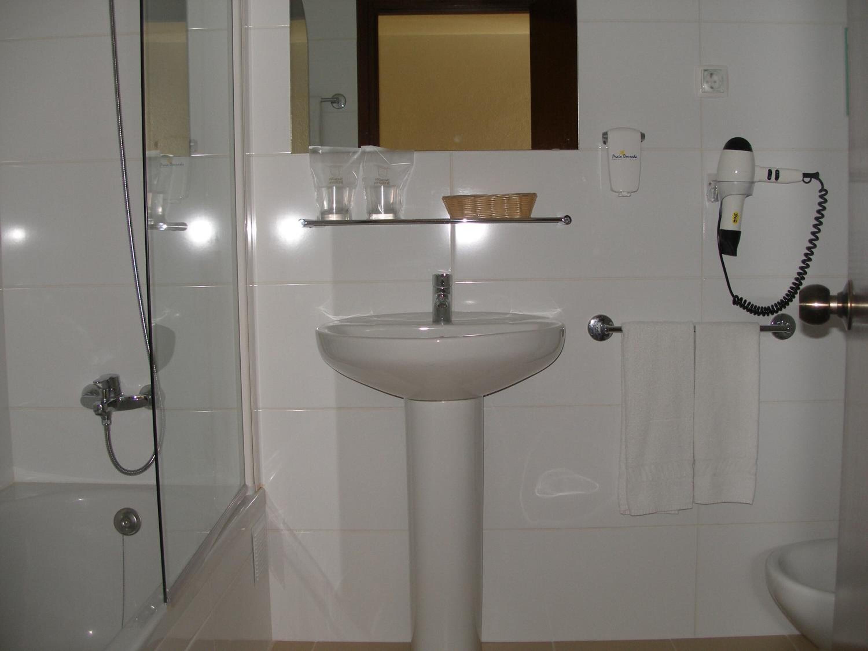 Une salle de bain avec une douche à parois de verre, un lavabo blanc, un miroir et un sèche-cheveux posé sur un support mural.