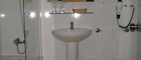 Une salle de bain avec une douche à parois de verre, un lavabo blanc, un miroir et un sèche-cheveux posé sur un support mural.
