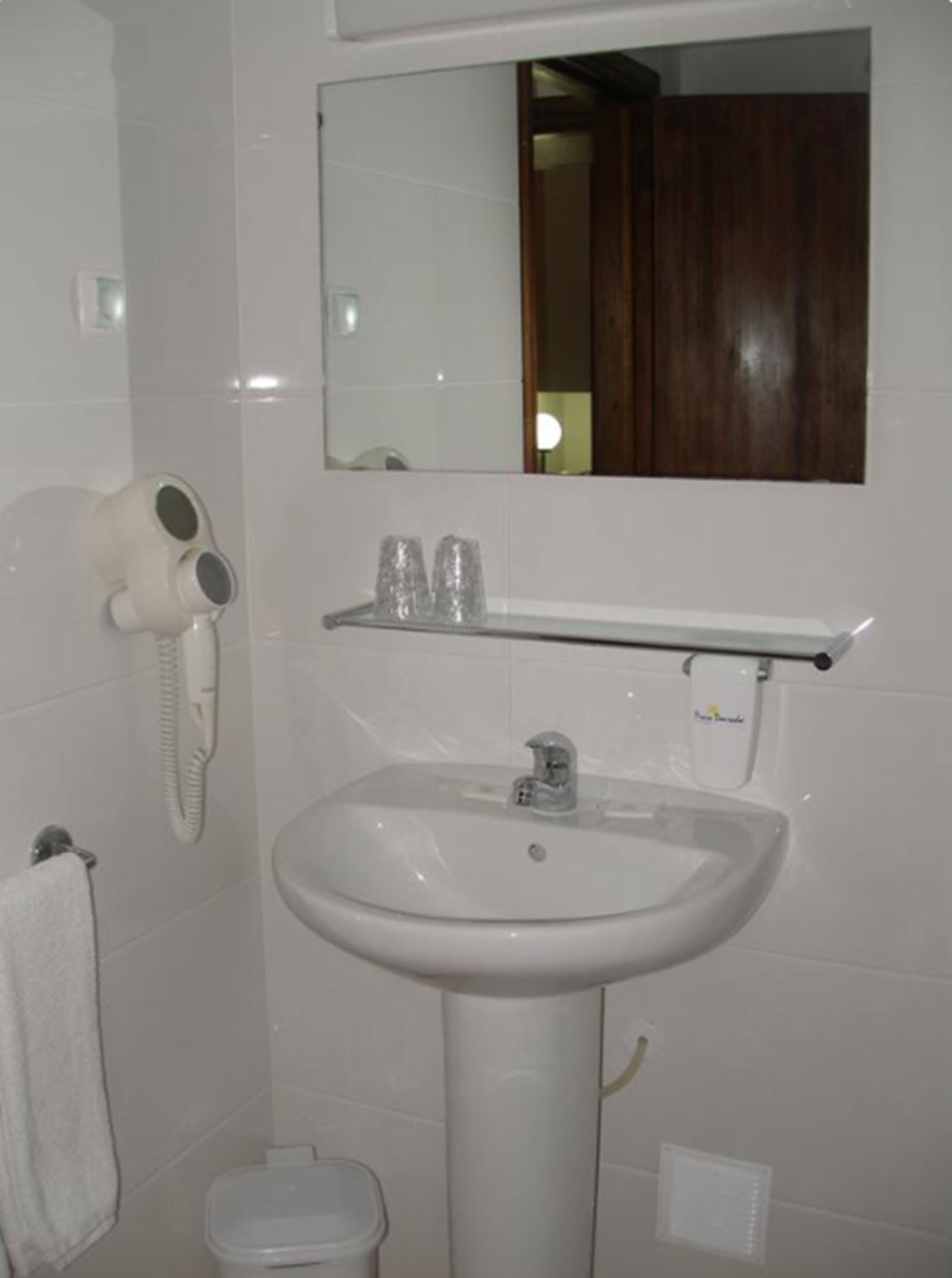 Un baño con lavamanos blanco, espejo, secador de pelo y retrete.