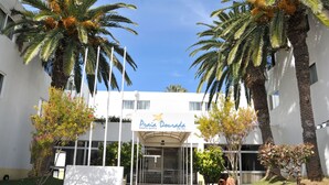 A hotel entrance with palm trees, a clear sky, and a sign reading "Praia Dourada Hotel". - Praia Dourada Hotel (Porto Santo)
