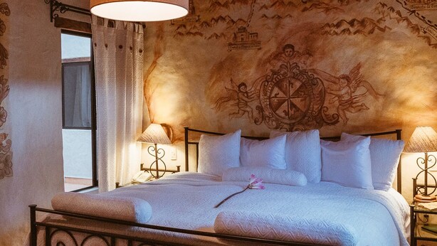 Ein Schlafzimmer mit einem Bett, zwei Nachttischen, einer Hängelampe und einer Wandweberei.
