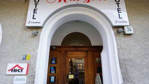 L'ingresso di un albergo chiamato 'Margrit Pension', con un arco in legno e una targa con il numero '24'.
