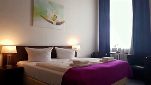 Una camera d'albergo con un letto, due lampade da comodino, una sedia, un tavolino e una finestra con tende.