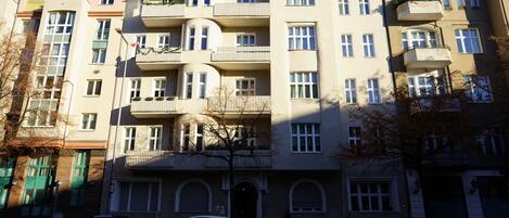 Un edificio residenziale a più piani con balconi, un ingresso centrale e auto parcheggiate davanti.