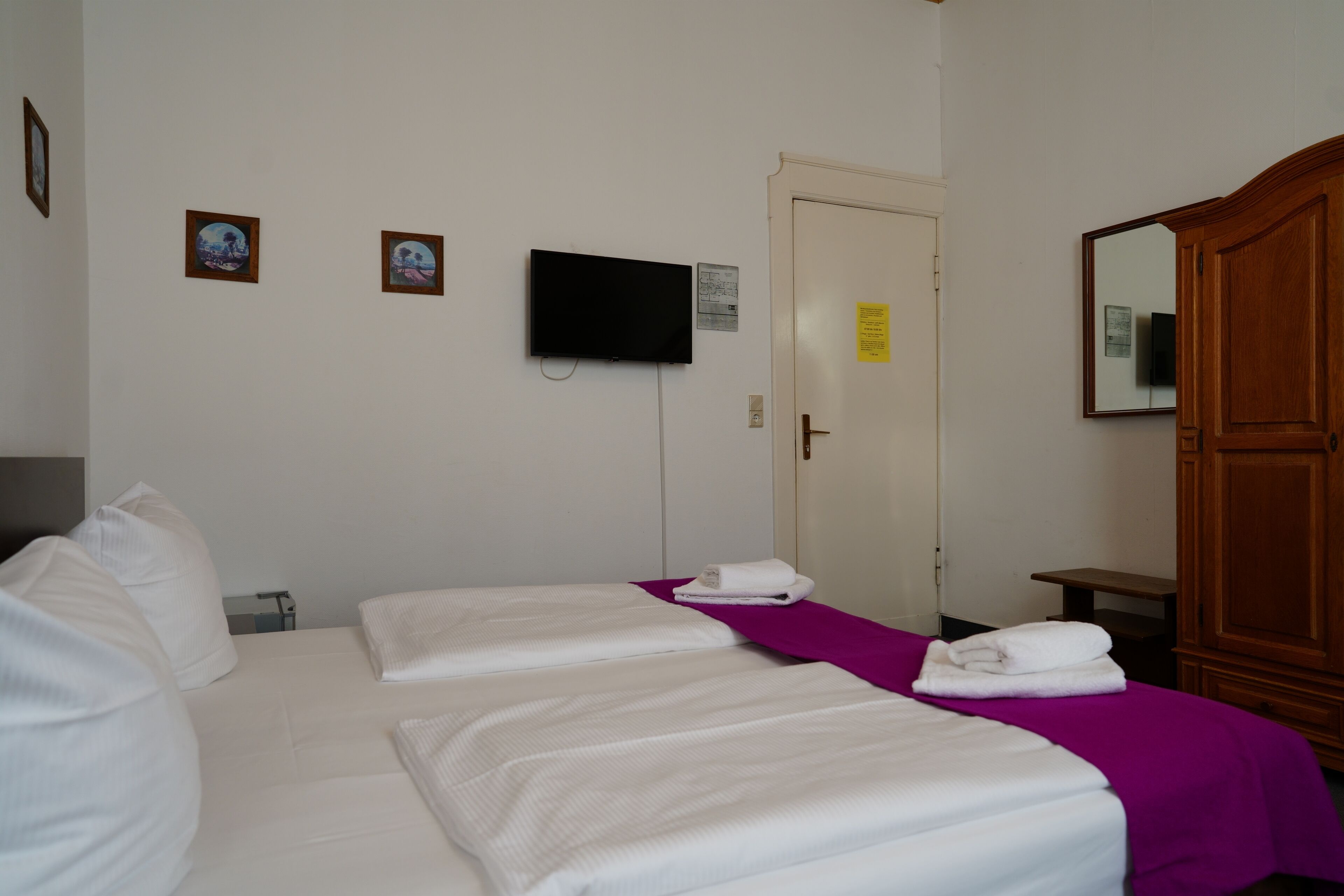 Habitación de hotel con dos camas, un televisor fijado a la pared y un armario de madera.