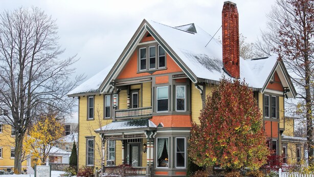 Ein zweistöckiges Haus mit rotem Dach, gelbem Farbanstrich und Schornstein.