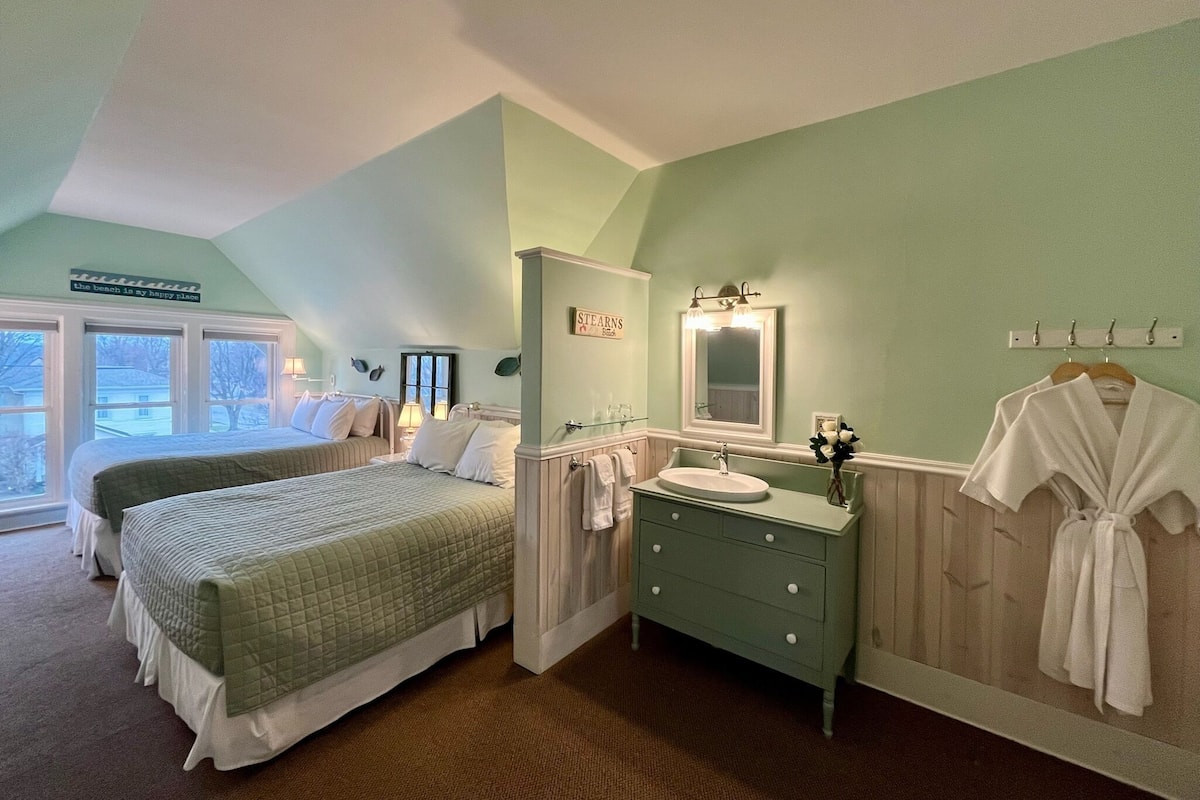 A bedroom with two beds, a vanity with a mirror, and a robe hanging on the wall.
