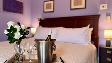 A hotel room with a bed, a tray with a bottle of champagne, two wine glasses, and a vase of white roses.