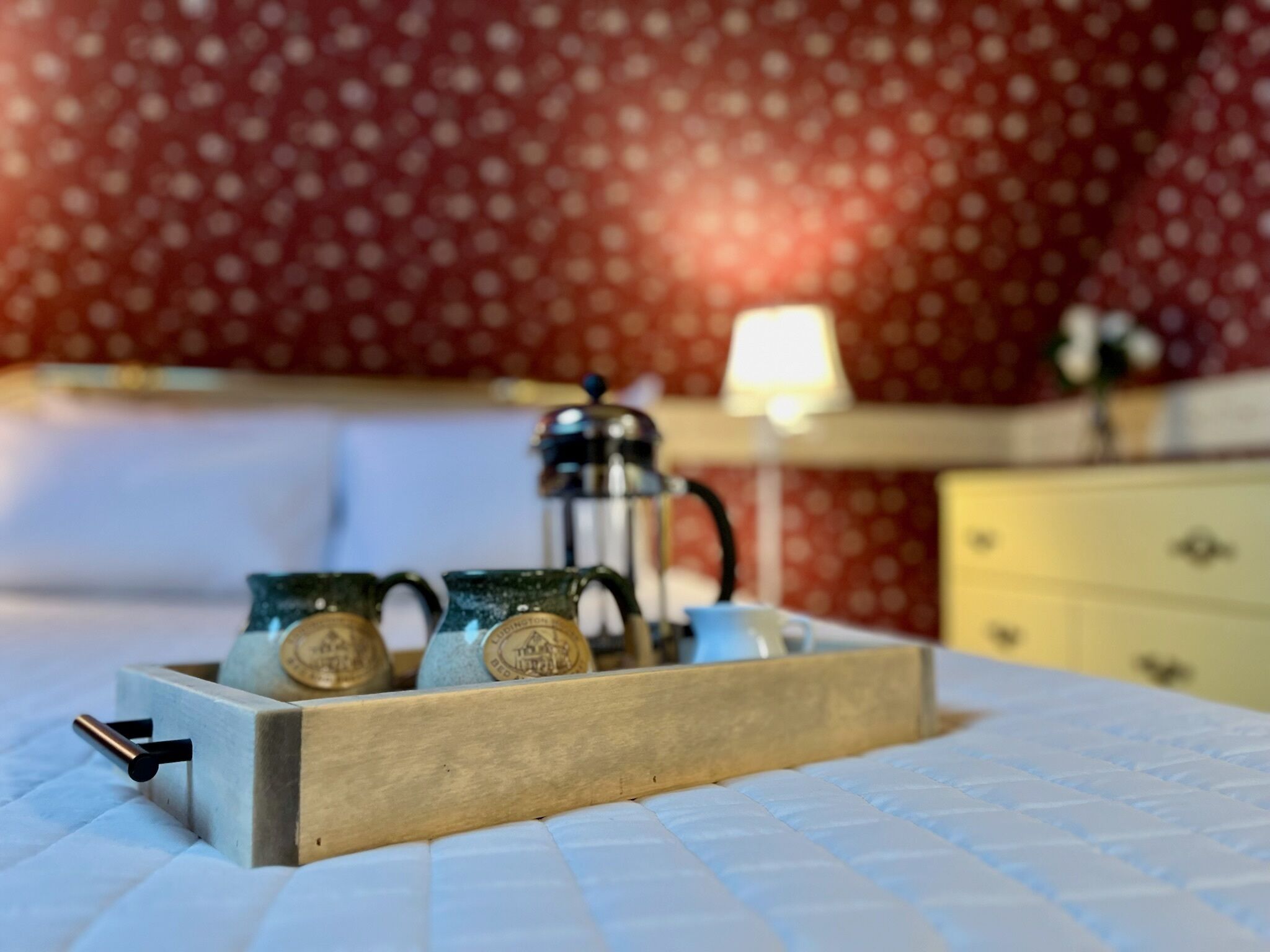 Una bandeja de madera con dos tazas de cerámica verde sobre una cama con cubierta azul acolchada.