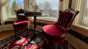 Ein Zimmer mit einem runden Tisch, zwei St ühlen und Blick auf Bäume durch ein Fenster.