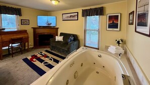 Ein Wohnzimmer mit Kamin, Fernseher, einer Couch und Badezuber, sowie gerahmten Bildern an den Wänden.