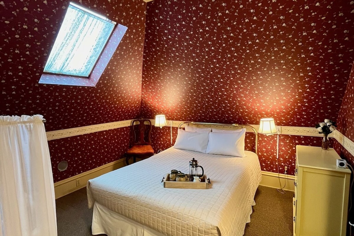 A hotel room with a bed, bedside lamps, a small table with a tray, a window, and a wardrobe.